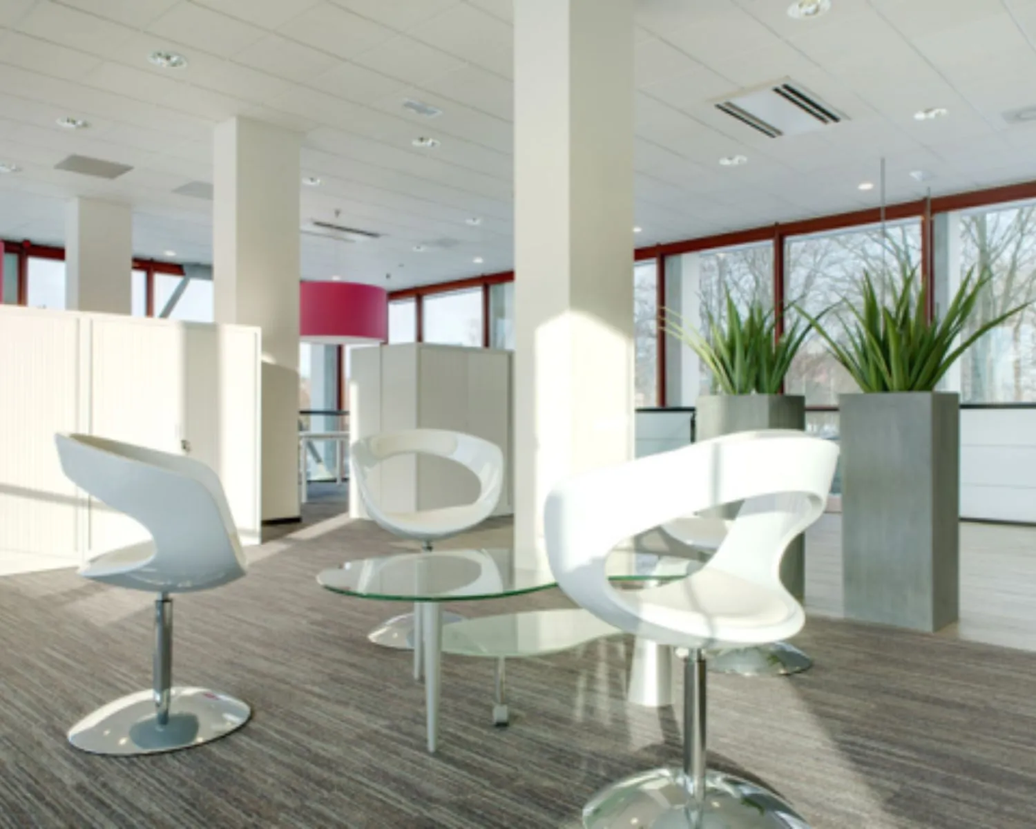 Moderne wachtruimte met witte designstoelen, glazen tafel en grote planten in een licht kantoorinterieur.
