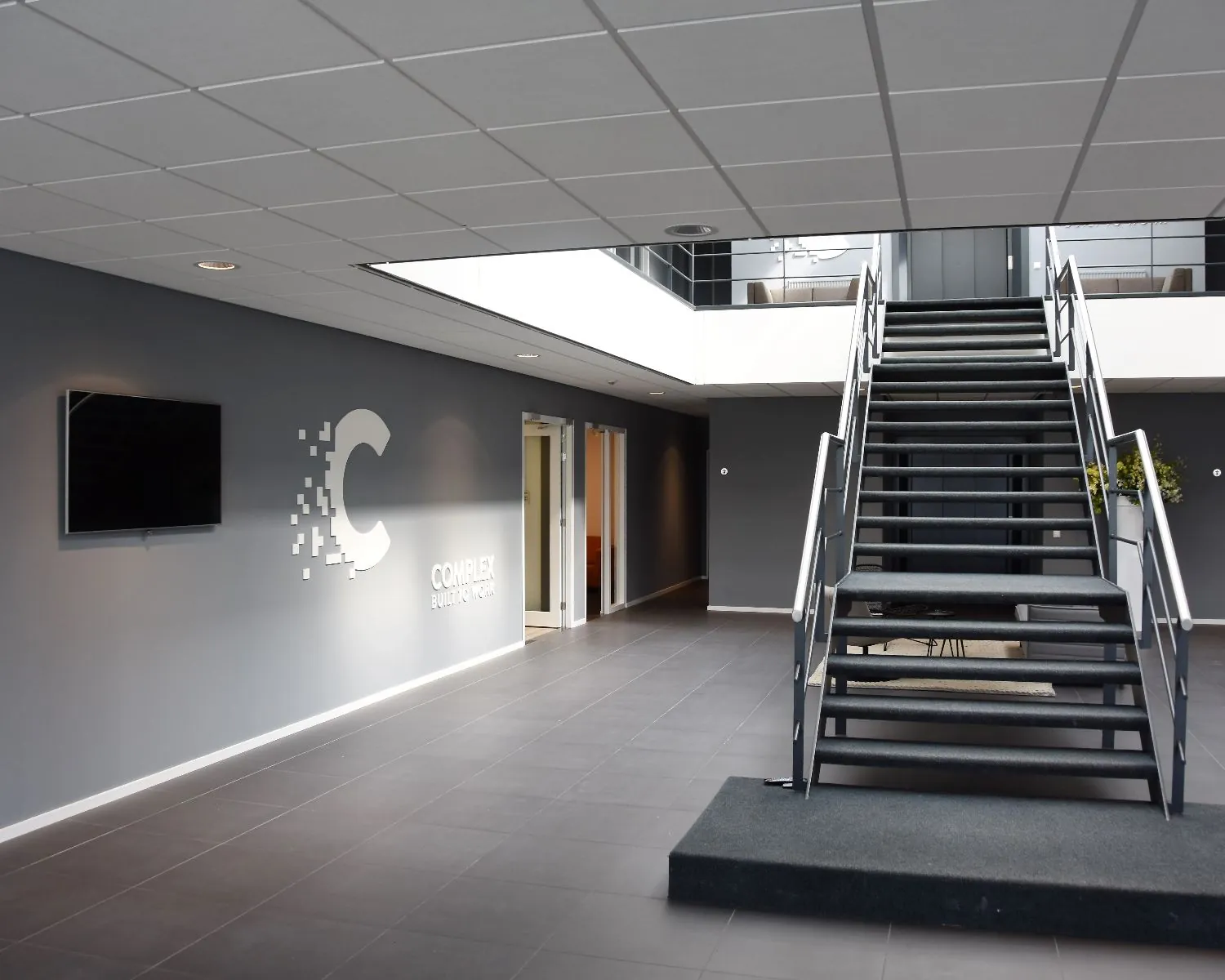 Moderne kantoorentree met een trap naar de bovenverdieping en het logo van Complex aan de muur.