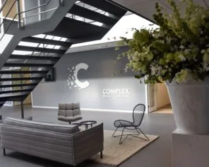 Moderne kantoorlobby met strakke meubels, een trap en het logo van Complex op de muur.