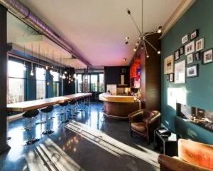 Moderne, sfeervol verlichte ruimte met lange bar, leren fauteuils en een open haard.