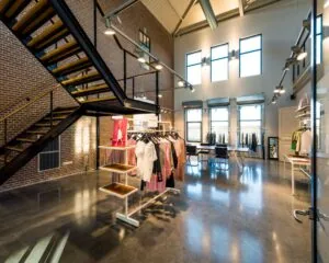 Moderne kledingwinkel met industriële inrichting, centraal rek met kleding en grote ramen die natuurlijk licht binnenlaten.