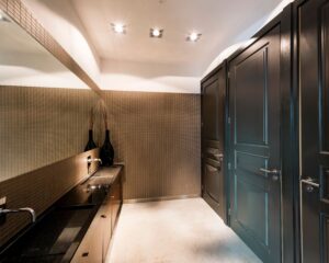 Moderne toiletruimte met donkere houten deuren, een lange wastafel met zwarte waskommen en een grote spiegel.