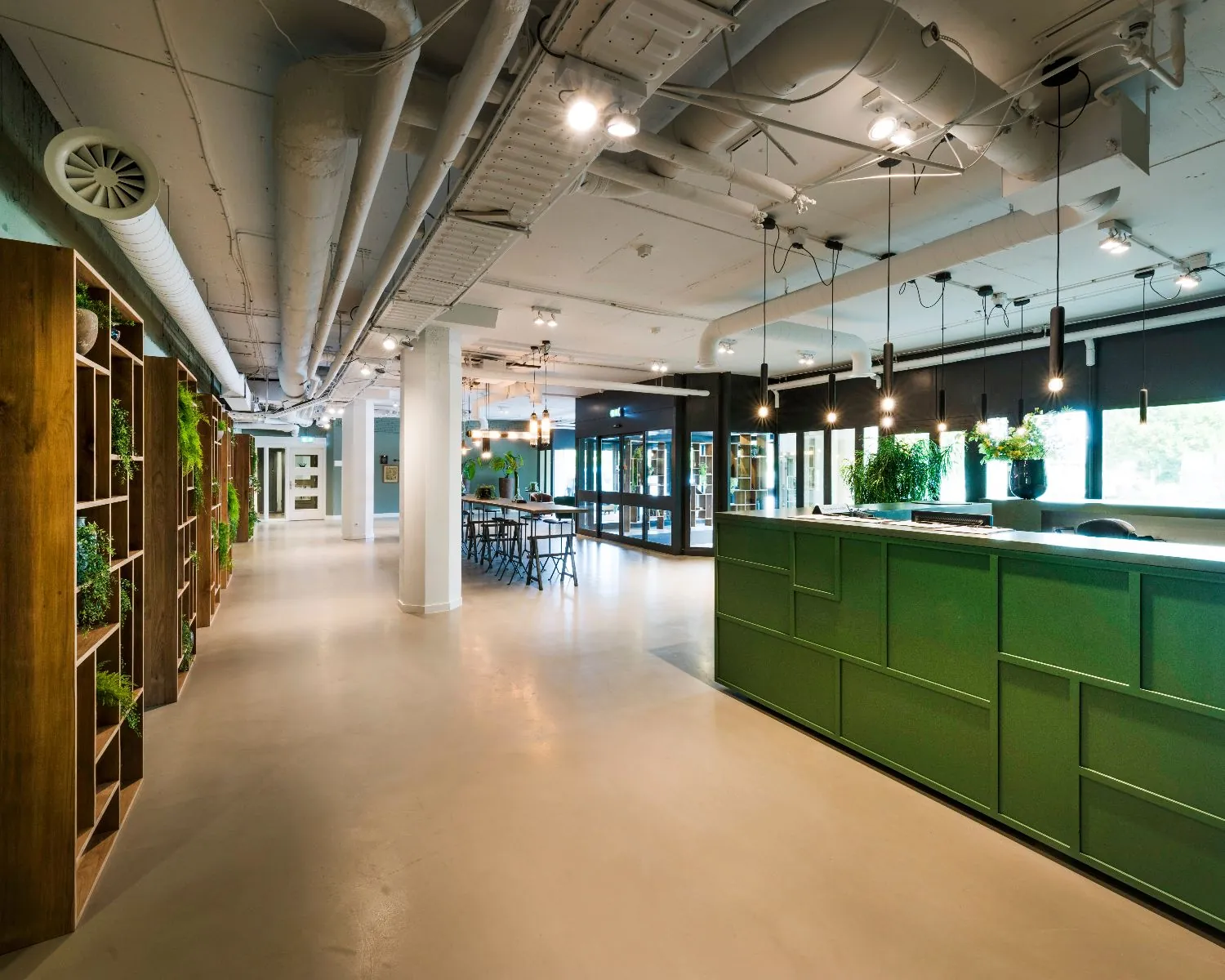 Moderne en open kantoorruimte met een groene receptiebalie, houten wandkasten met planten en industriële plafonddetails.