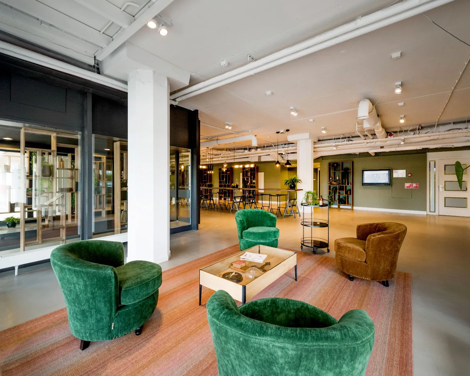 Moderne en stijlvolle loungehoek met groene en bruine fauteuils rondom een houten salontafel op een zachtgekleurd vloerkleed.