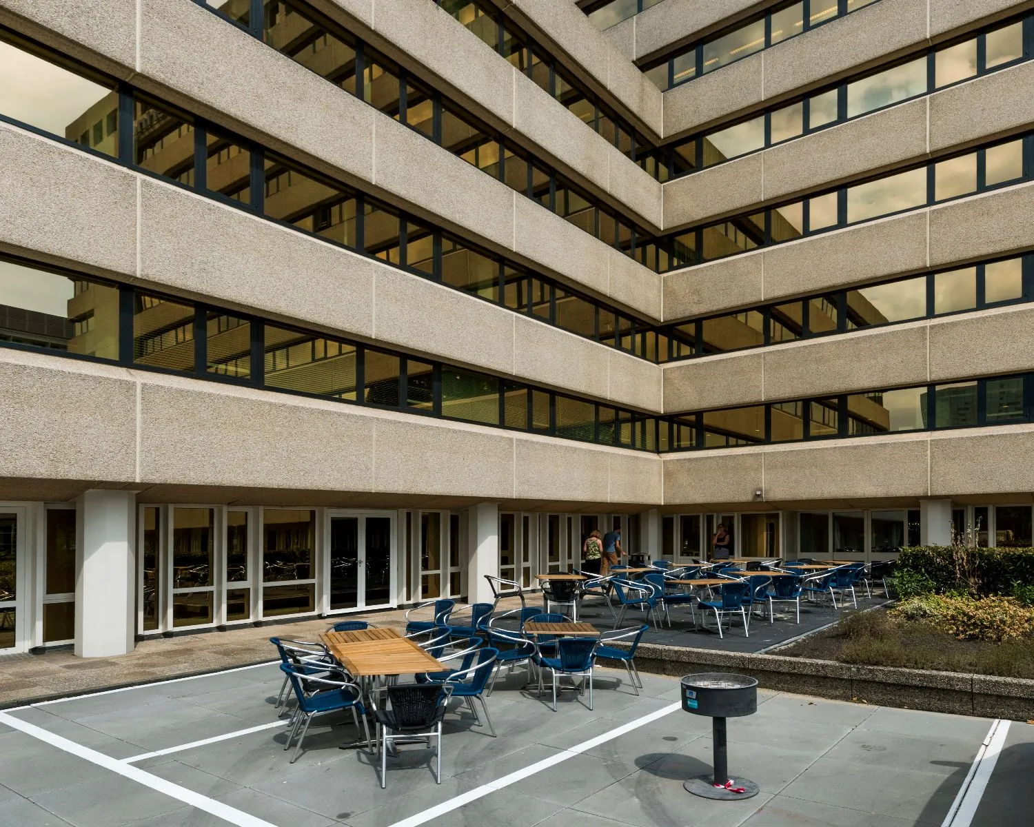 Binnenplein met tafels en stoelen tussen de gevels van een modern kantoorgebouw.