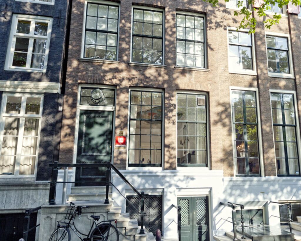 Voorgevel van het Anne Frank Huis in Amsterdam met grote ramen en een trap met een fiets ervoor.