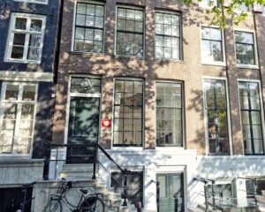 Voorgevel van het Anne Frank Huis in Amsterdam met grote ramen en een trap met een fiets ervoor.
