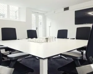 Moderne vergaderruimte met een witte tafel, zwarte bureaustoelen en een flatscreen aan de muur.