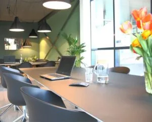 Moderne vergaderruimte met een lange tafel, laptops, bloemenvaas en hanglampen.