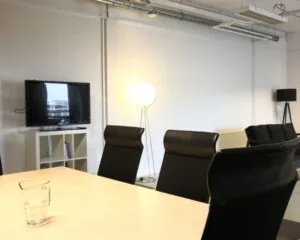 Moderne vergaderruimte met zwarte stoelen, een houten tafel, een tv aan de muur en sfeerverlichting.