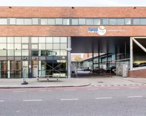 Voorgevel van het bedrijfsverzamelgebouw Kaap Noord aan de Asterweg met glazen entree, parkeerplaatsen en fietsenstalling onder een overkapping.