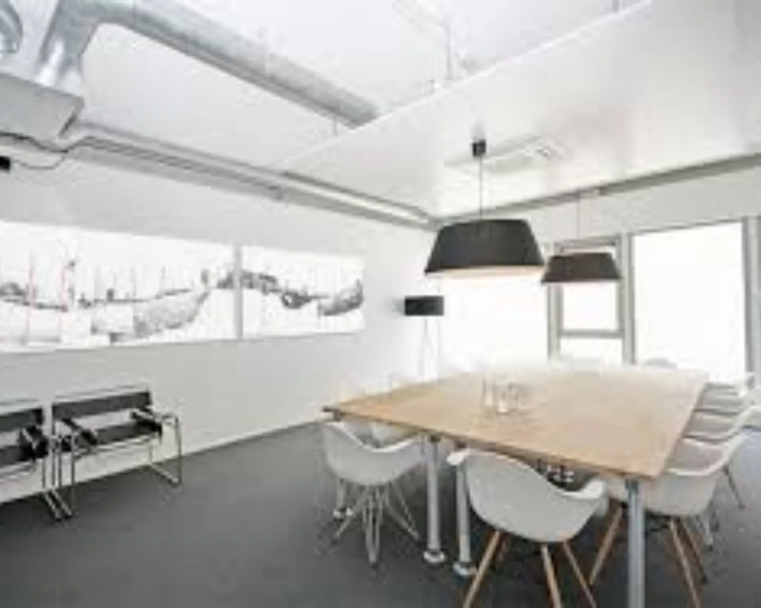 Moderne vergaderruimte met een houten tafel, witte stoelen, industriële plafondbuizen en zwart-witte kunst aan de muur.
