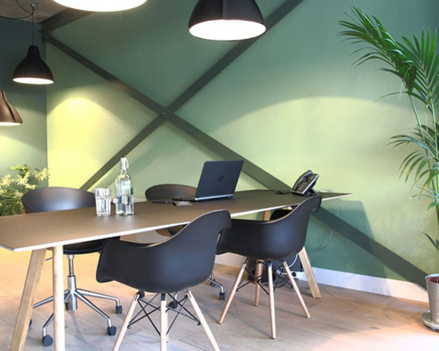 Moderne vergaderruimte met zwarte stoelen, een houten tafel, laptop en groene wanddecoratie.