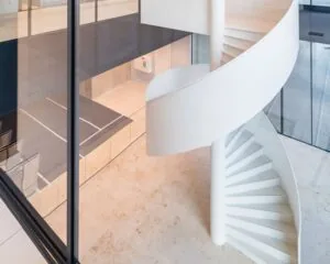 Witte wenteltrap in een modern interieur met glazen wanden en lichte tegelvloer.