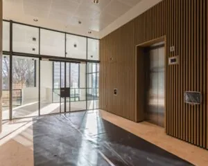 Moderne, lichte entreehal met een lift, houten wandbekleding en glazen draaideuren.