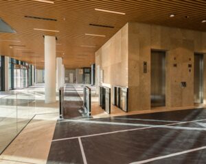 Moderne kantoorentree met houten plafond, glazen draaipoortjes en liften in een natuurstenen wand.