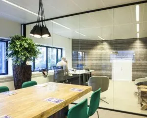 Moderne kantoorruimte met glazen wanden, een houten vergadertafel en een man die aan een bureau werkt.