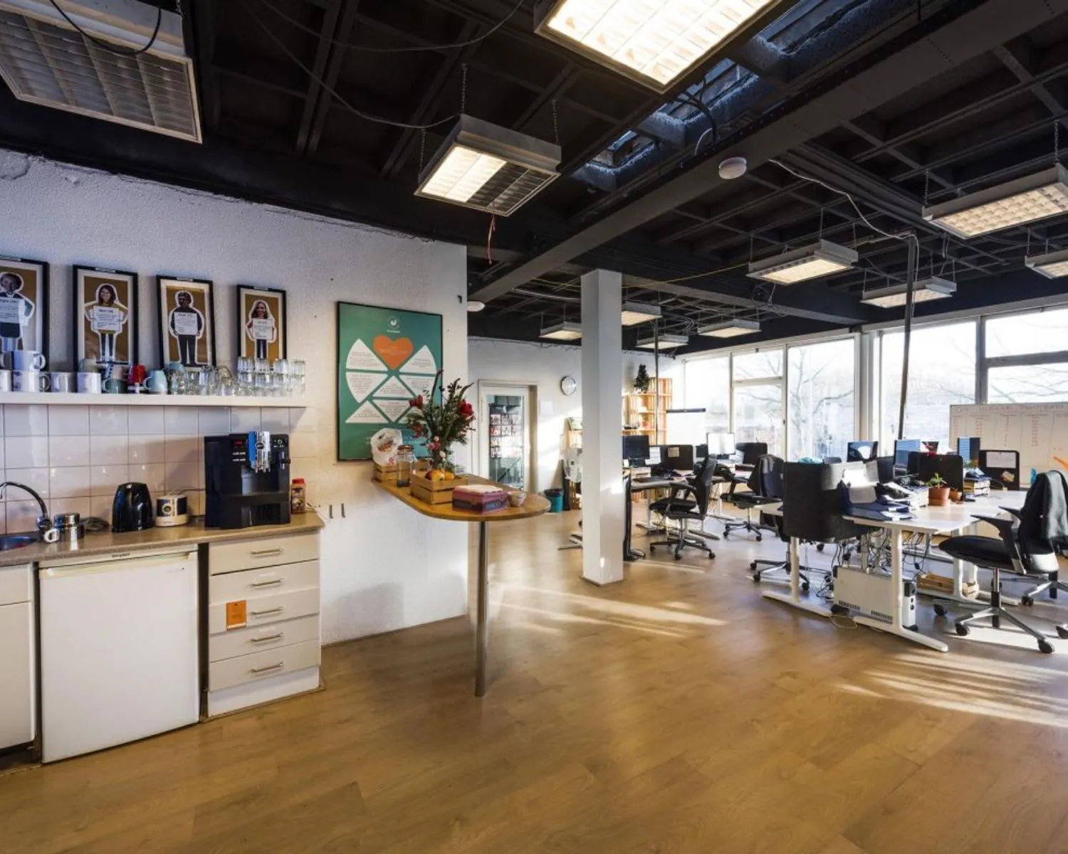 Open en modern kantoor met een koffiehoek, bloemen op een tafel en meerdere werkplekken met bureaustoelen en computers.