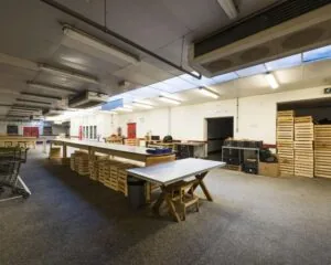 Binnenruimte met lange sorteertafels, houten kratten en industriële verlichting, vermoedelijk in een distributie- of verpakkingsruimte.