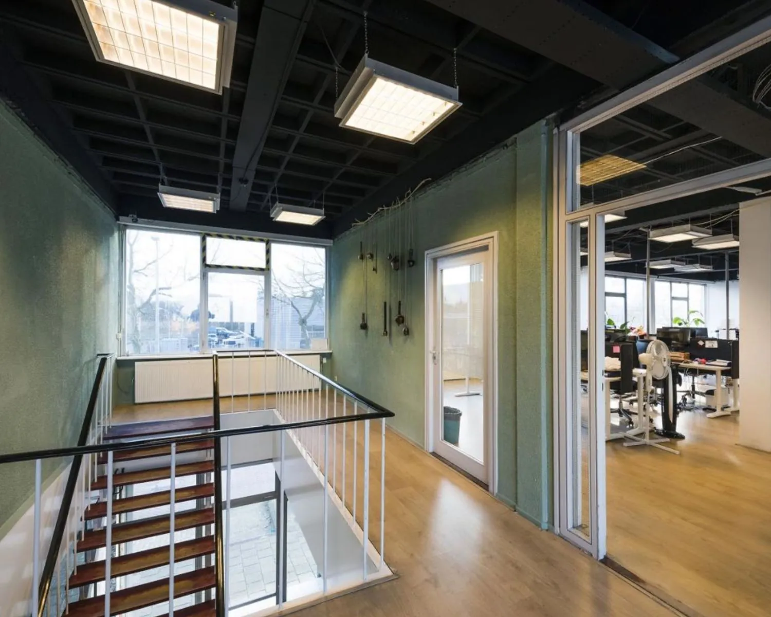 Moderne kantoorruimte met houten trap, glazen deur en open werkplekken met bureaus en computers.