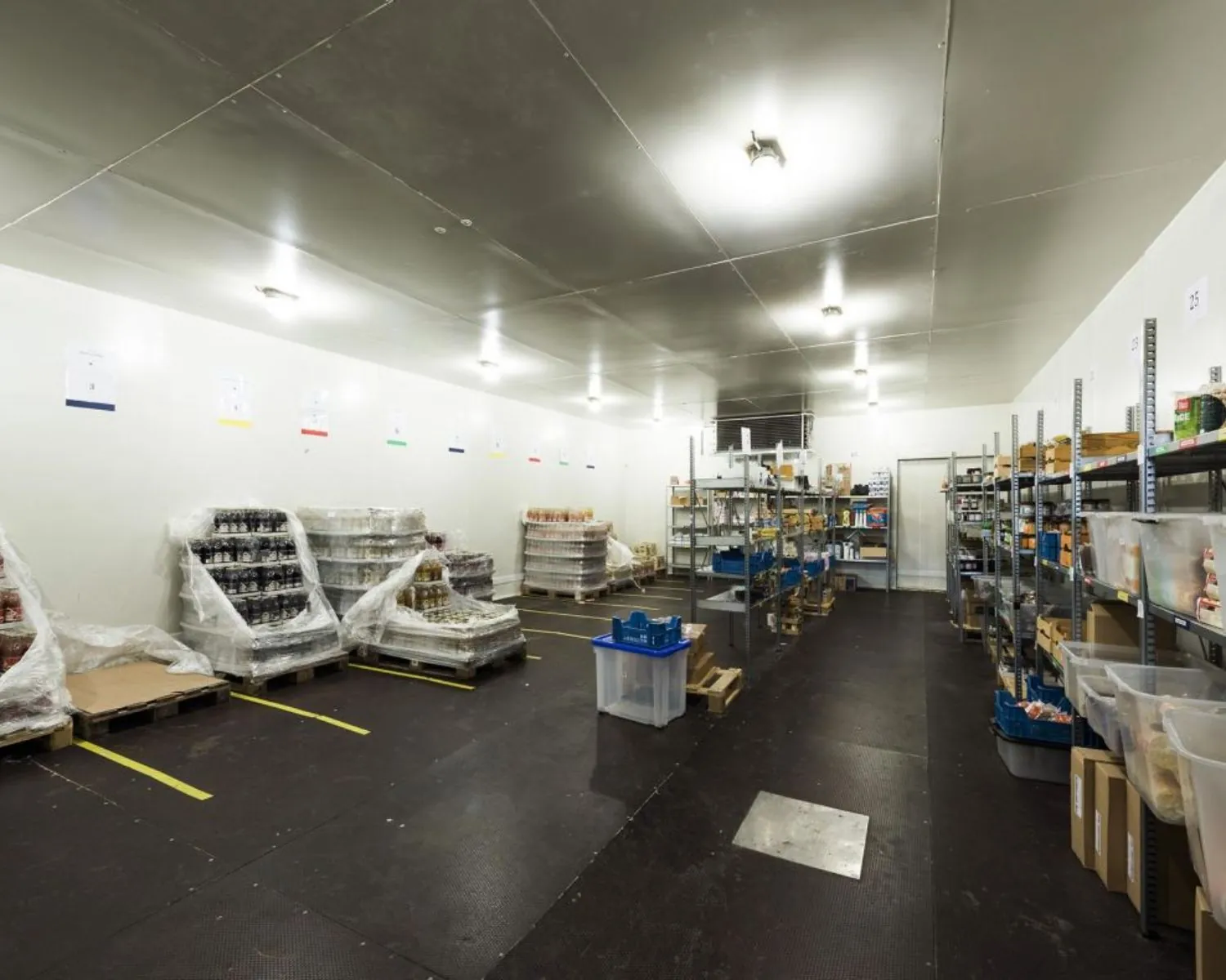 Opslagruimte met metalen rekken en pallets vol verpakte voedingsmiddelen in een koelmagazijn.