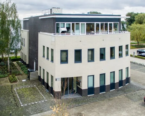 Modern kantoorgebouw met lichte gevel, zwarte accenten en grote ramen, gelegen aan een rustige straat.