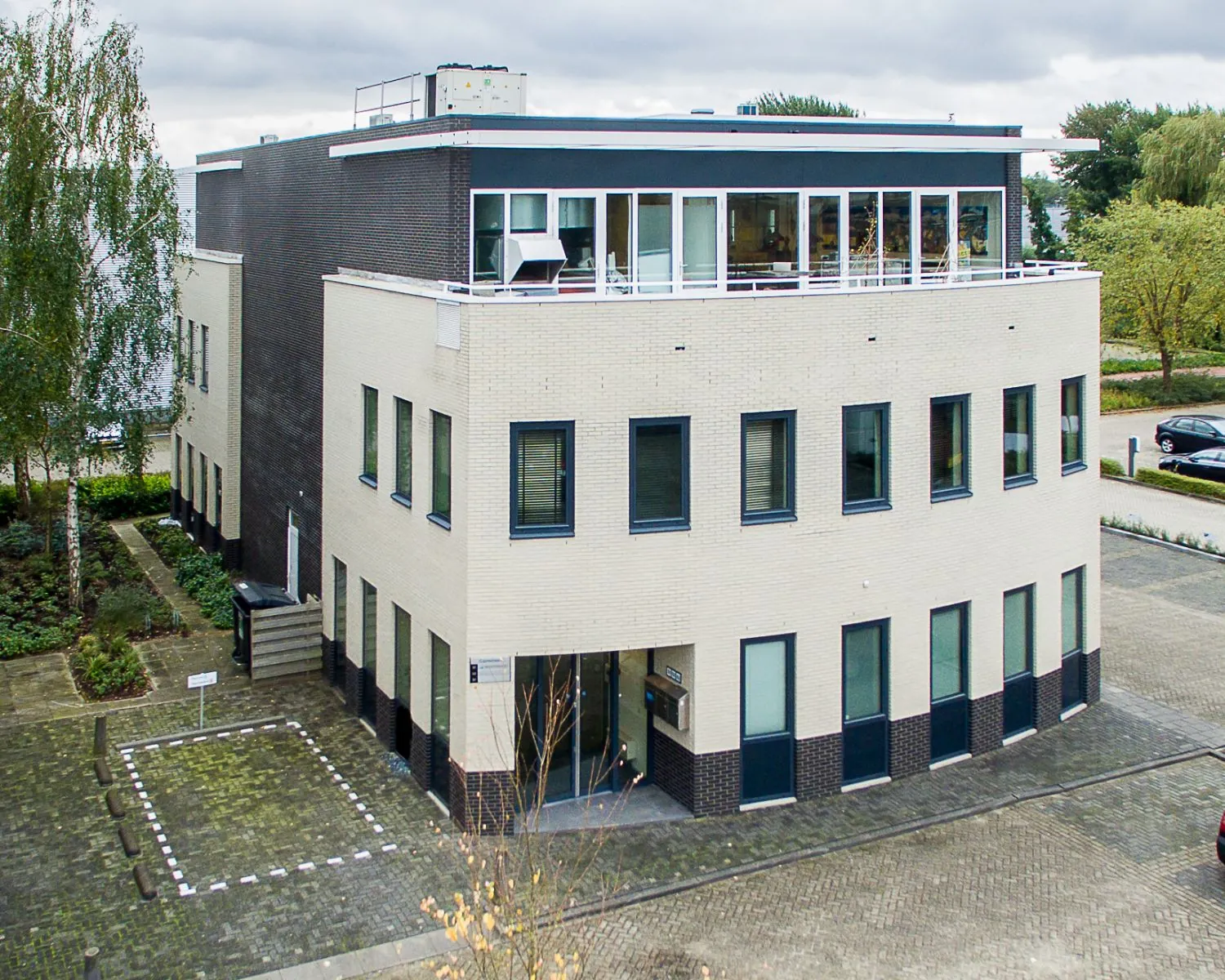 Modern kantoorgebouw met lichte gevel, zwarte accenten en grote ramen, gelegen aan een rustige straat.