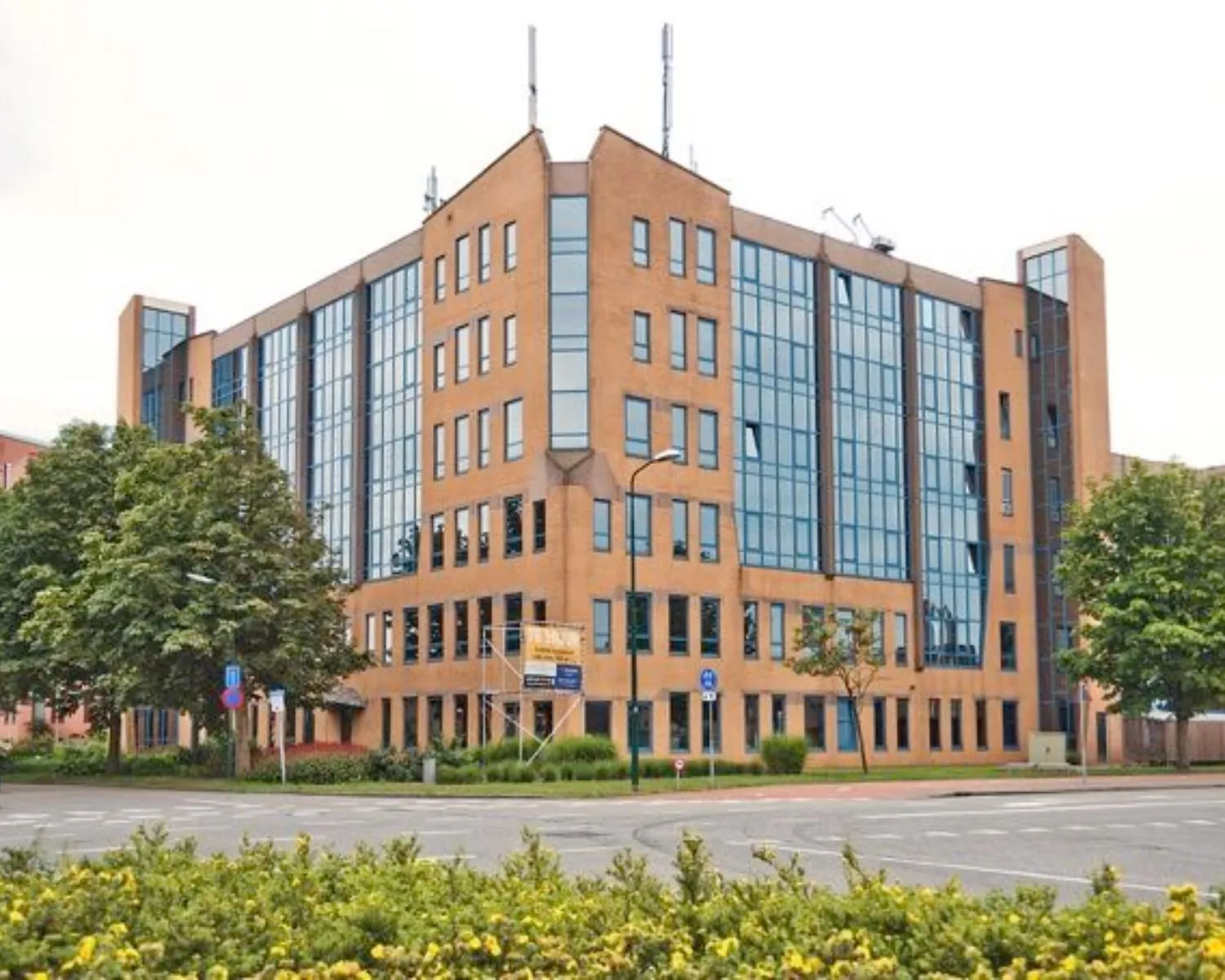 Kantoorgebouw met gevels van roodbruin metselwerk en grote raampartijen aan een kruispunt.