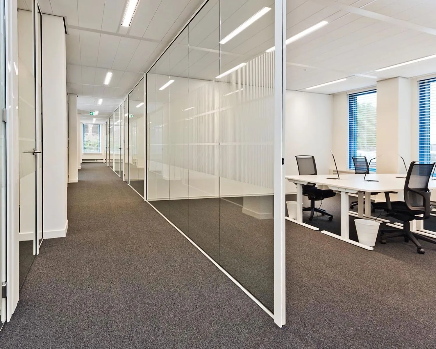 Moderne kantoorruimte met glazen wanden, bureaus en ergonomische bureaustoelen.