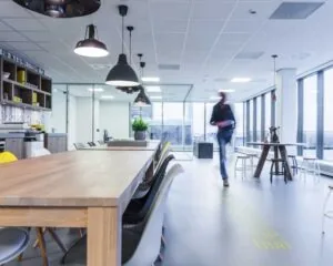Moderne open kantoorruimte met houten tafels, designstoelen en een persoon die voorbijloopt.