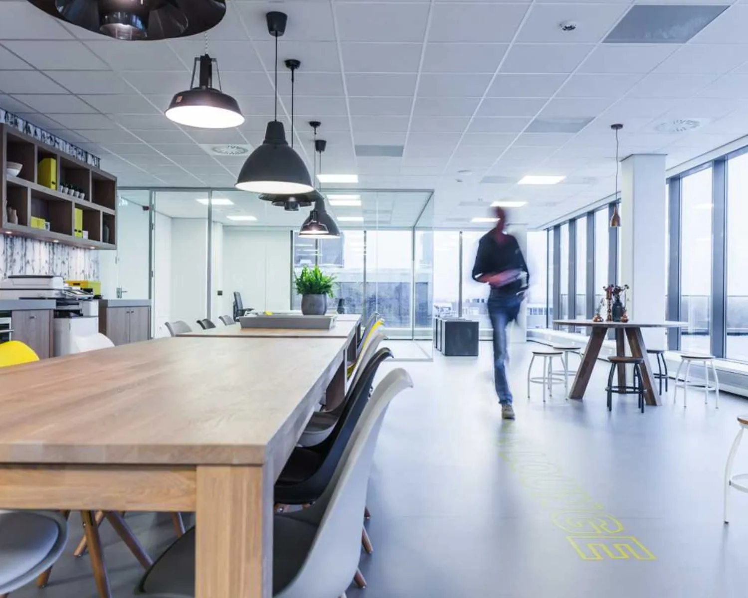 Moderne open kantoorruimte met houten tafels, designstoelen en een persoon die voorbijloopt.