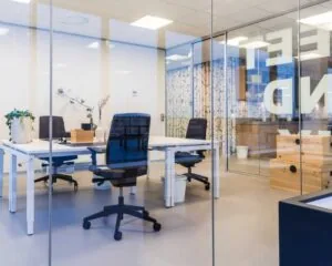 Moderne glazen kantoorruimte met minimalistische inrichting, bureaus, bureaustoelen en planten.
