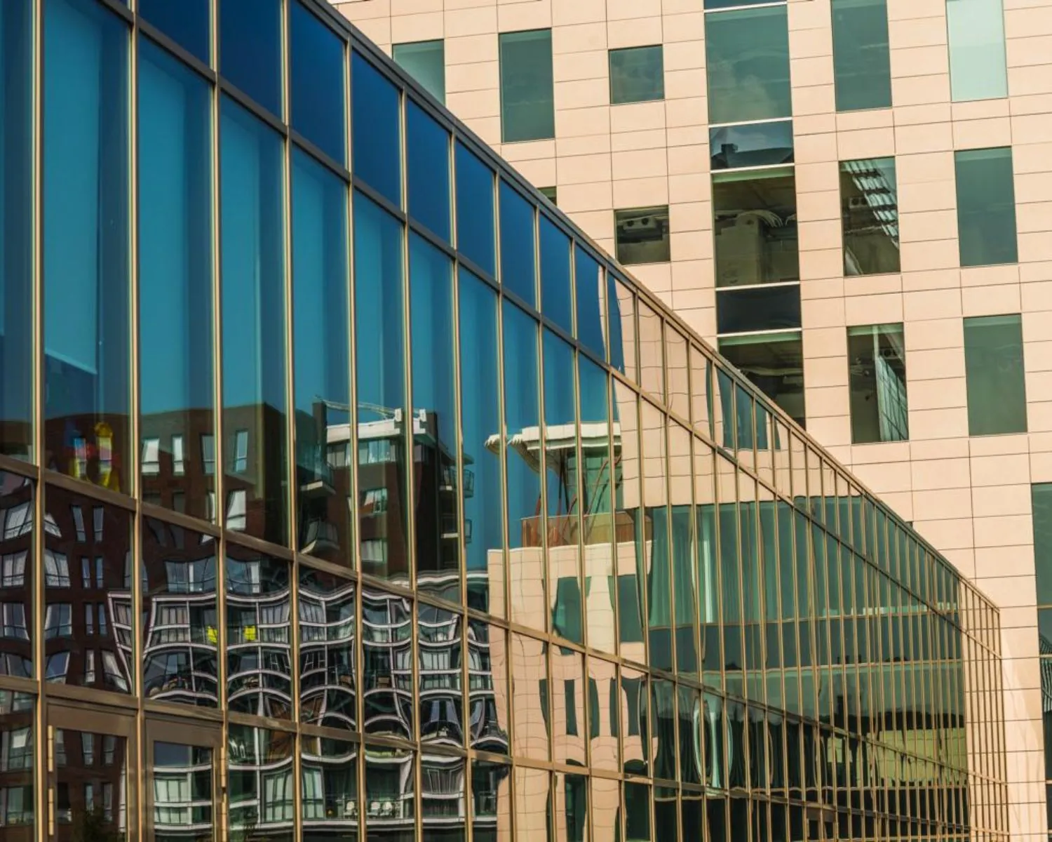 Glazen gevel van een modern gebouw met reflectie van een tegenoverliggende architectonisch complex.