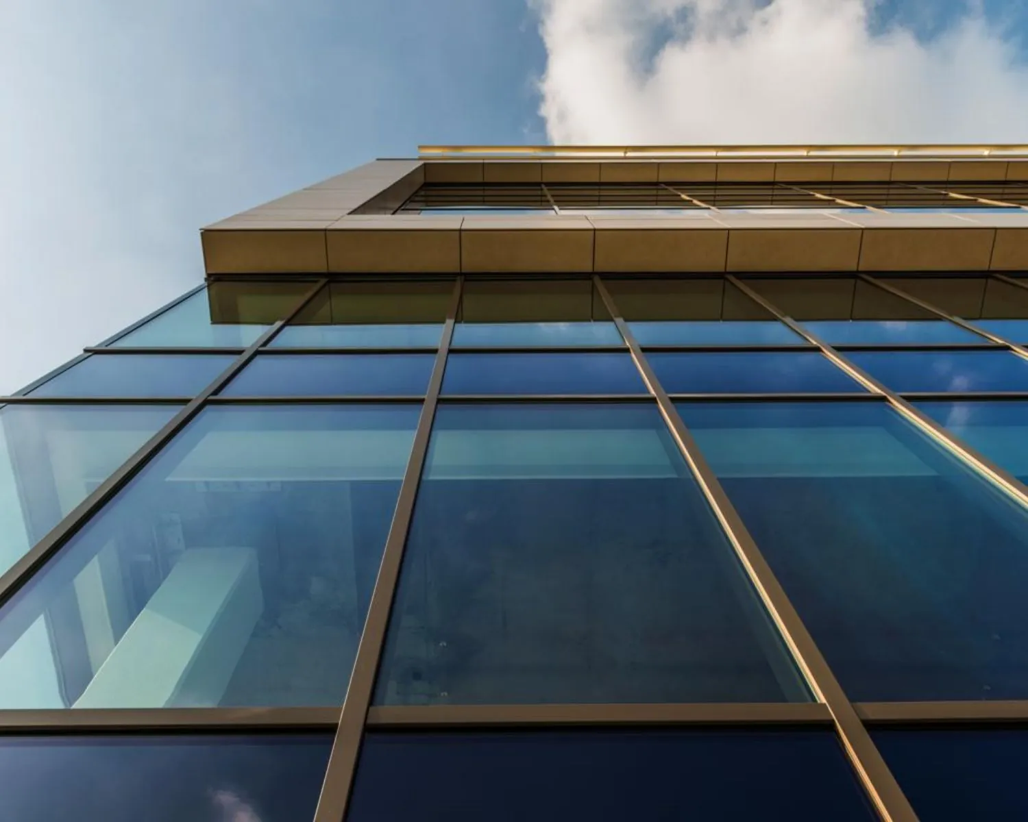 Laaghoekopname van een modern kantoorgebouw met grote glazen ramen en een blauwe lucht op de achtergrond.