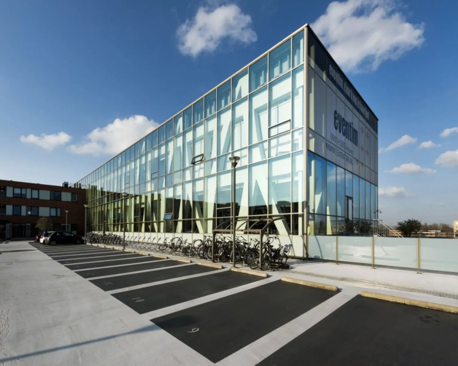 Glazen kantoorgebouw van Eventim met fietsenstalling en parkeerplaatsen op de voorgrond.