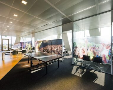 Modern kantoorinterieur met een pingpongtafel en vergaderruimtes met glazen wanden voorzien van festivalfoto's.