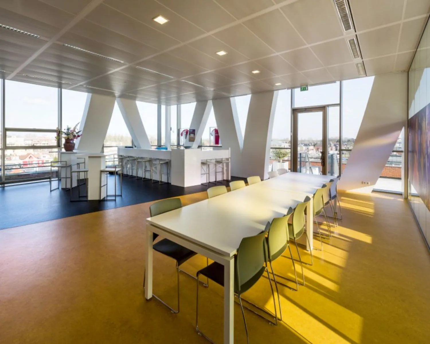 Moderne, lichtovergoten kantineruimte met lange vergadertafel, barkrukken en panoramisch uitzicht.
