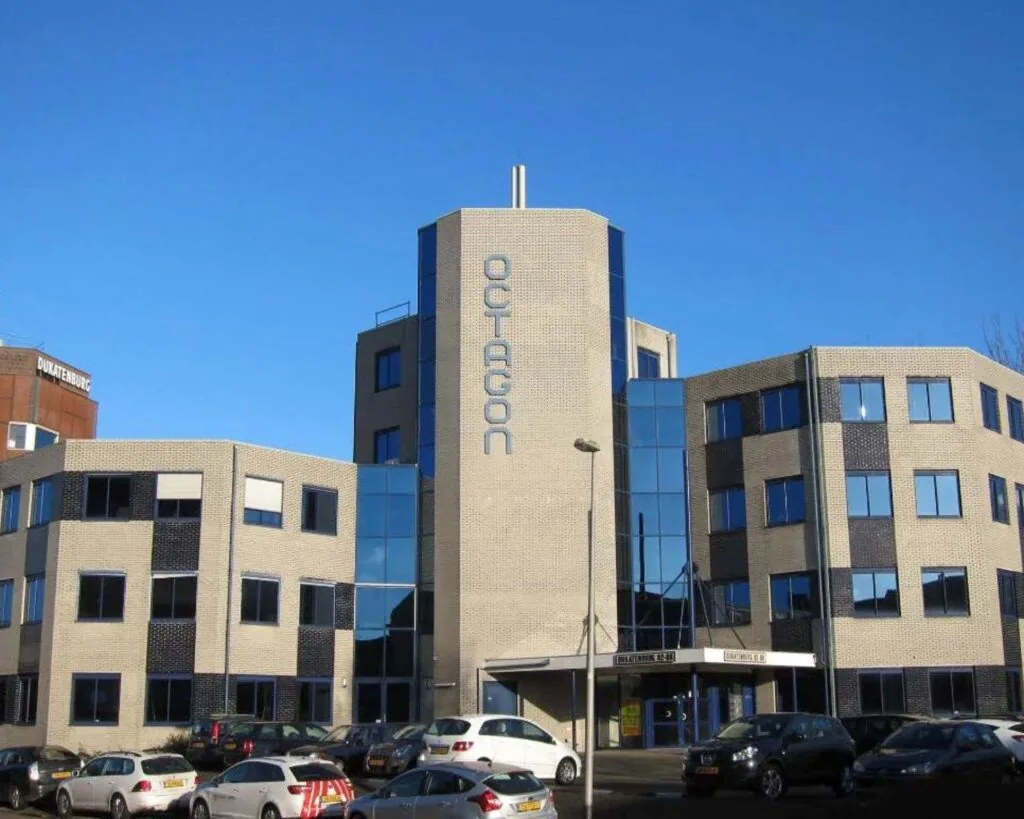 Kantoorgebouw Octagon met beige bakstenen gevel en blauwe ramen, gelegen aan een parkeerterrein.