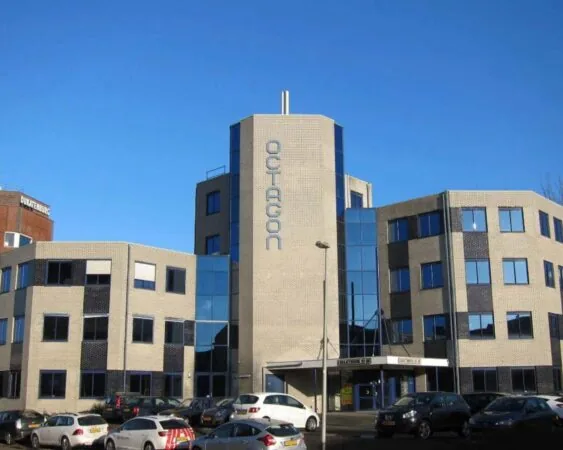 Kantoorgebouw Octagon met beige bakstenen gevel en blauwe ramen, gelegen aan een parkeerterrein.