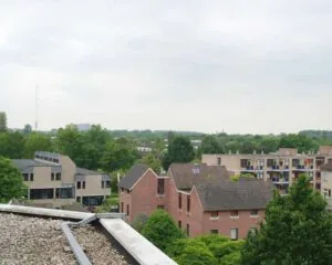 Uitzicht op een woonwijk met rode bakstenen huizen, moderne appartementsgebouwen en veel groen onder een bewolkte lucht.