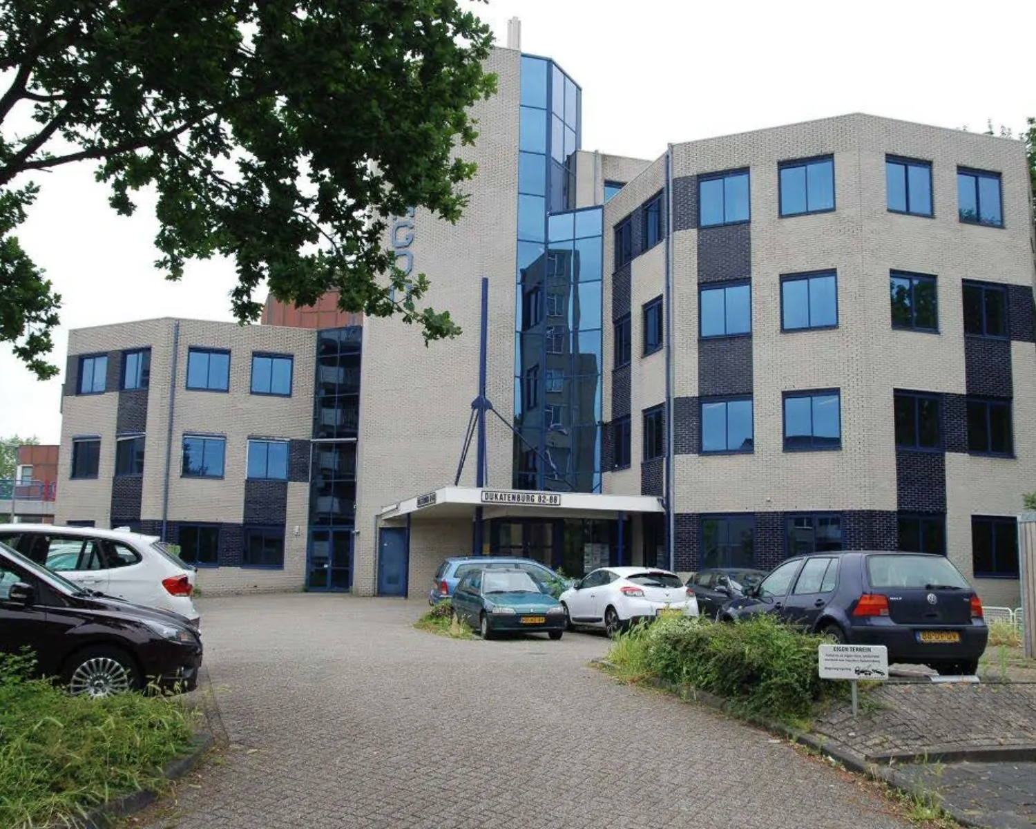 Kantoorgebouw met glazen entree aan de Dukatenburg 2-80 in Nieuwegein, omgeven door geparkeerde auto’s.