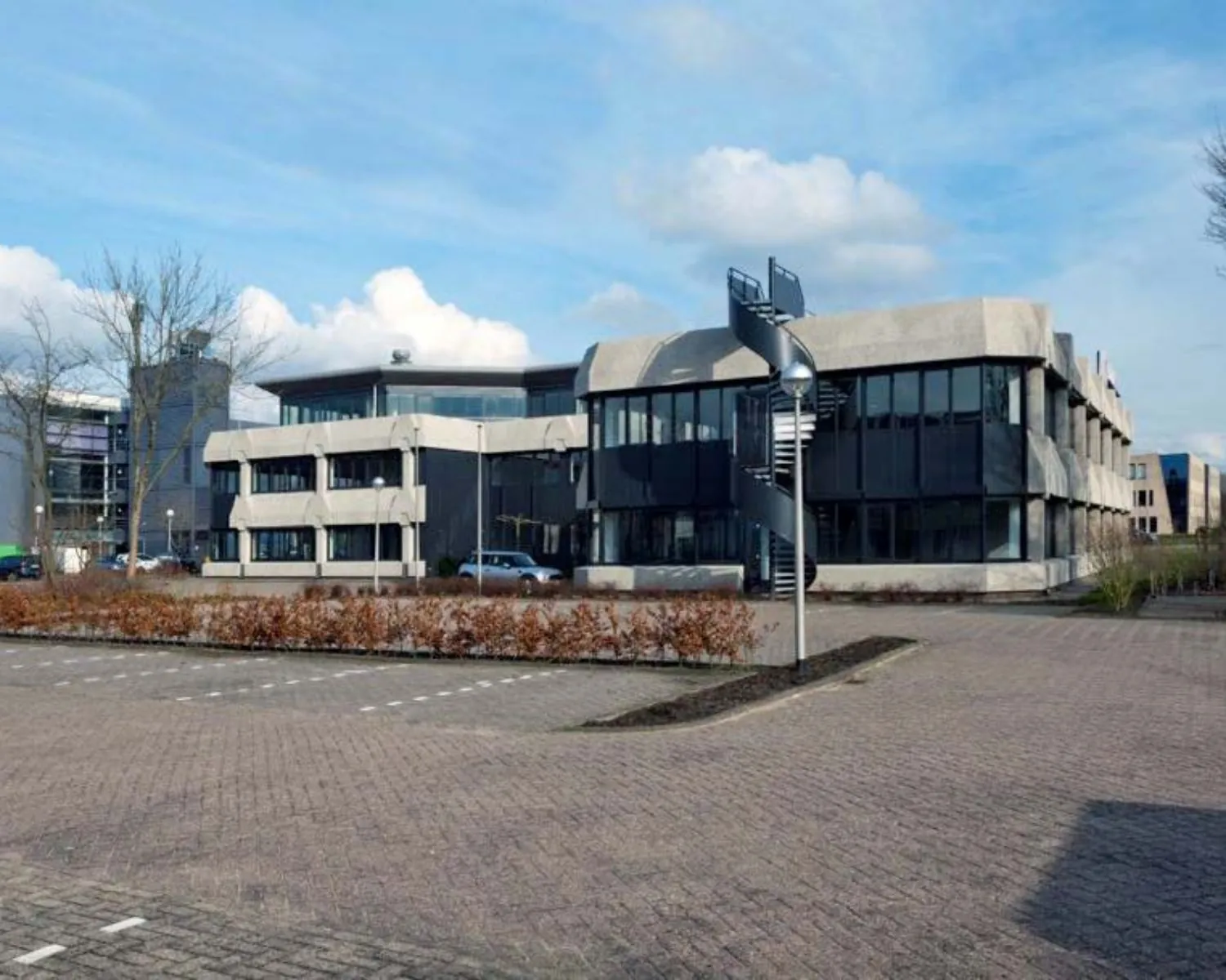 Modern kantoorpand met opvallende buitentrap en lege parkeerplaatsen op de voorgrond.