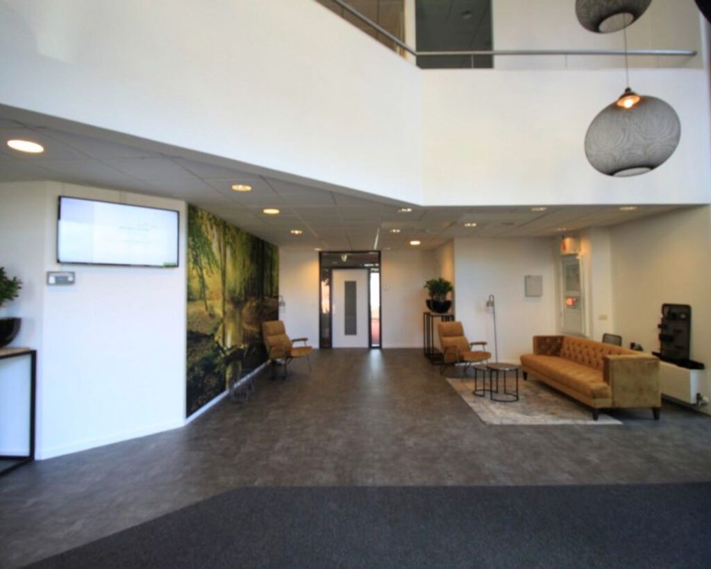 Moderne kantoorentree met zithoek, muurdecoratie van een boslandschap en een flatscreen aan de muur.