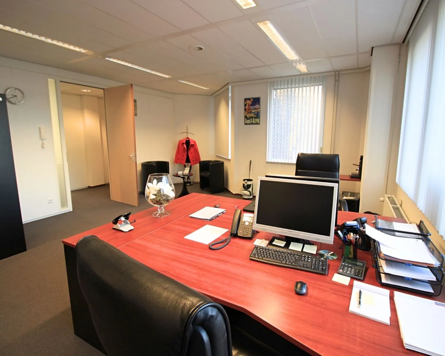 Modern ingericht kantoor met een groot houten bureau, computer en leren bureaustoelen.