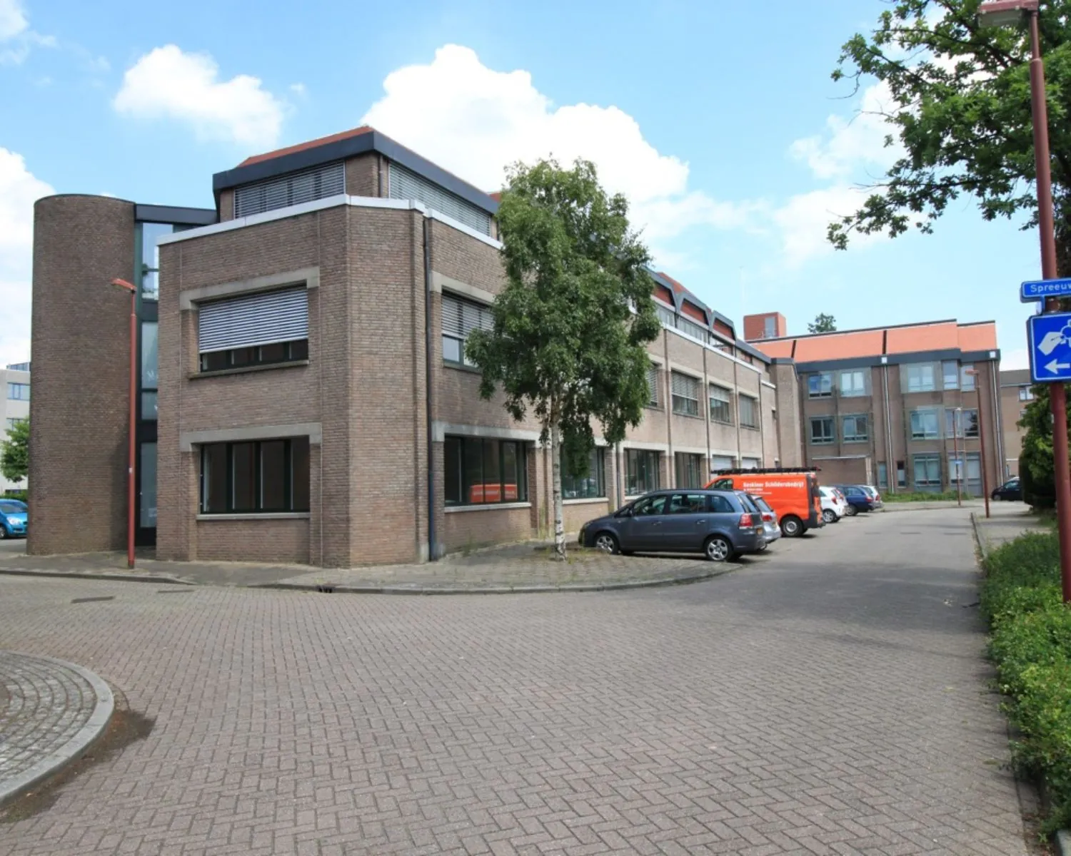 Bakstenen kantoorgebouw met meerdere verdiepingen en parkeerplaatsen aan de Spreeuwenstraat.