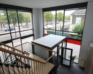 Interieur van een modern trappenhuis met grote ramen en uitzicht op een stadsstraat met fietsen en auto's.