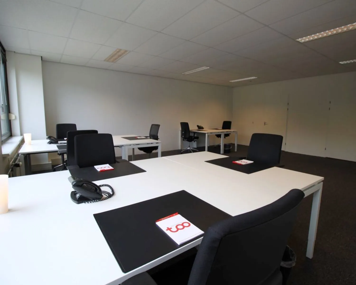 Moderne, ruime kantoorruimte met meerdere bureaus, stoelen, telefoons en notitieblokken met het logo "TOO".