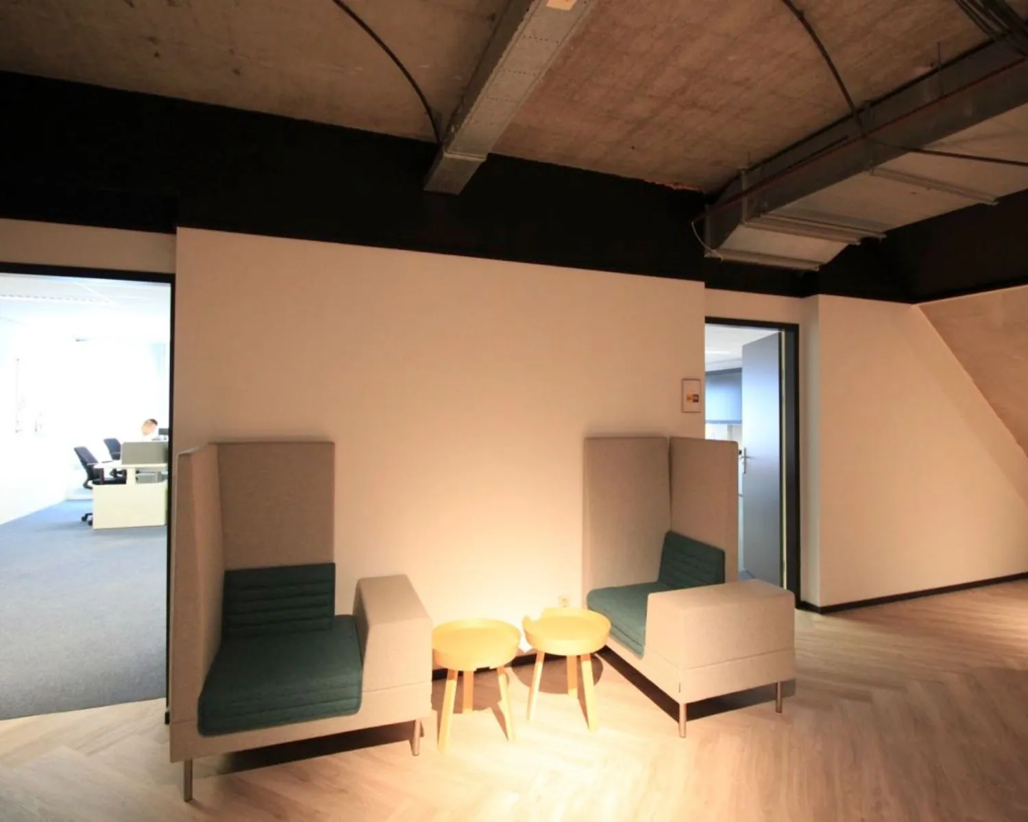 Twee moderne fauteuils met hoge rugleuning en twee houten bijzettafels staan in een minimalistische kantoorruimte met houten vloer.