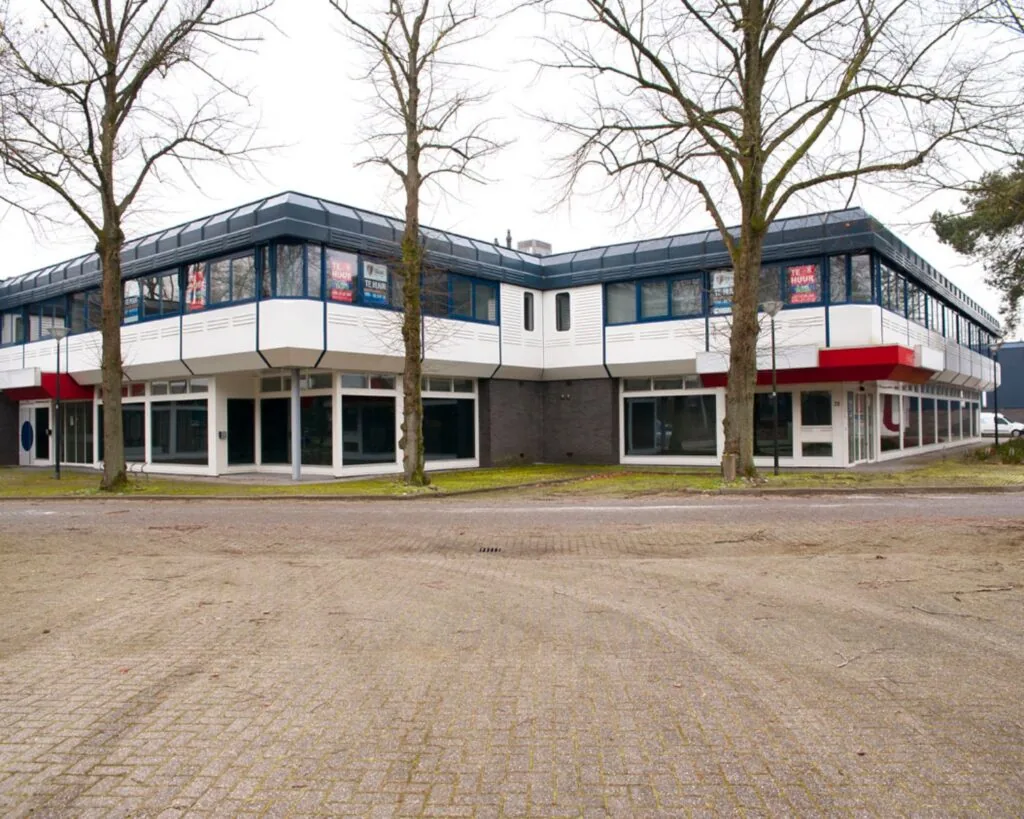Twee verdiepingen tellend kantoorpand met te huur-borden in de ramen, omringd door bomen en een lege parkeerplaats.