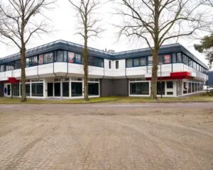 Twee verdiepingen tellend kantoorpand met te huur-borden in de ramen, omringd door bomen en een lege parkeerplaats.